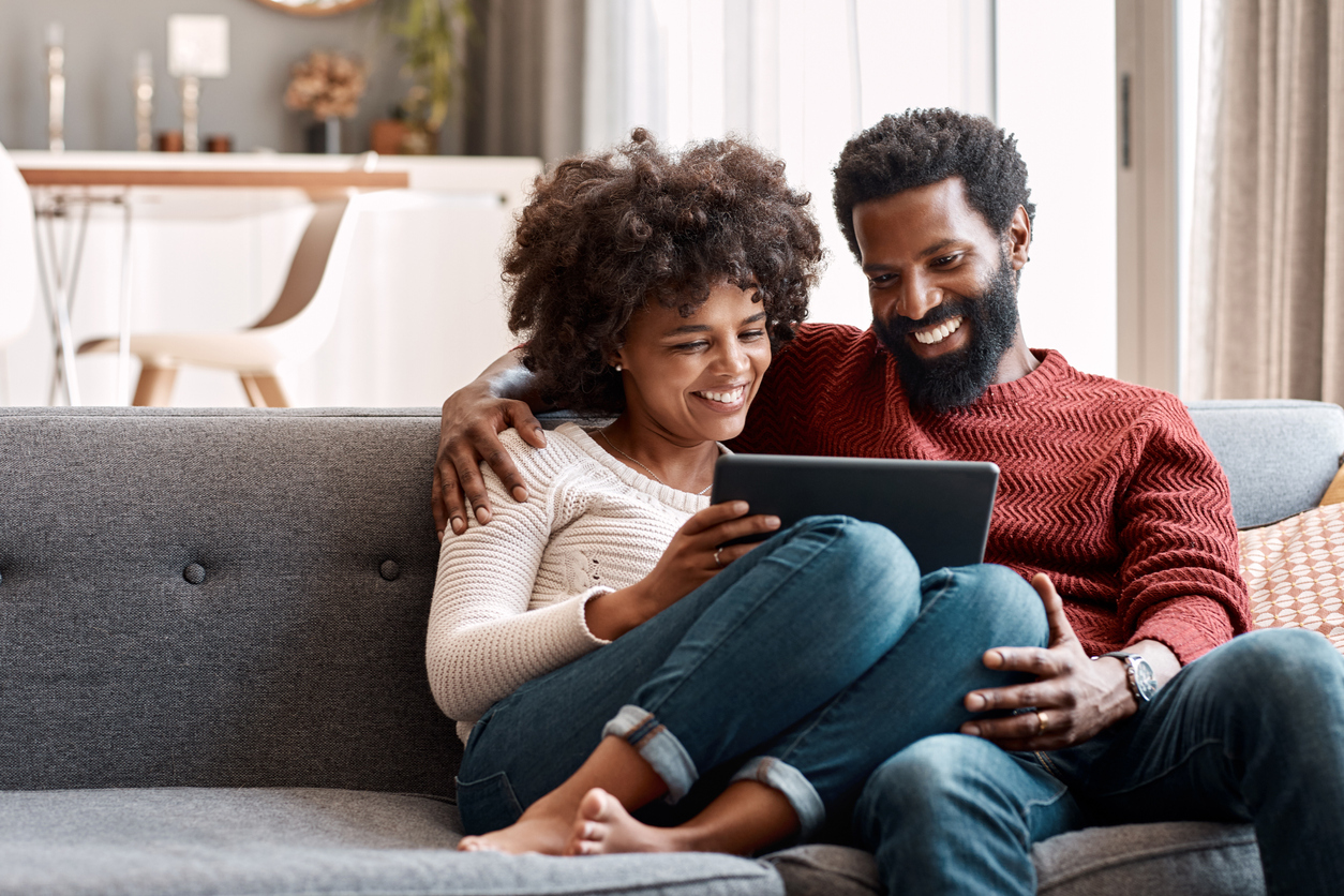 Happy couple sitting on couch smiling at tablet